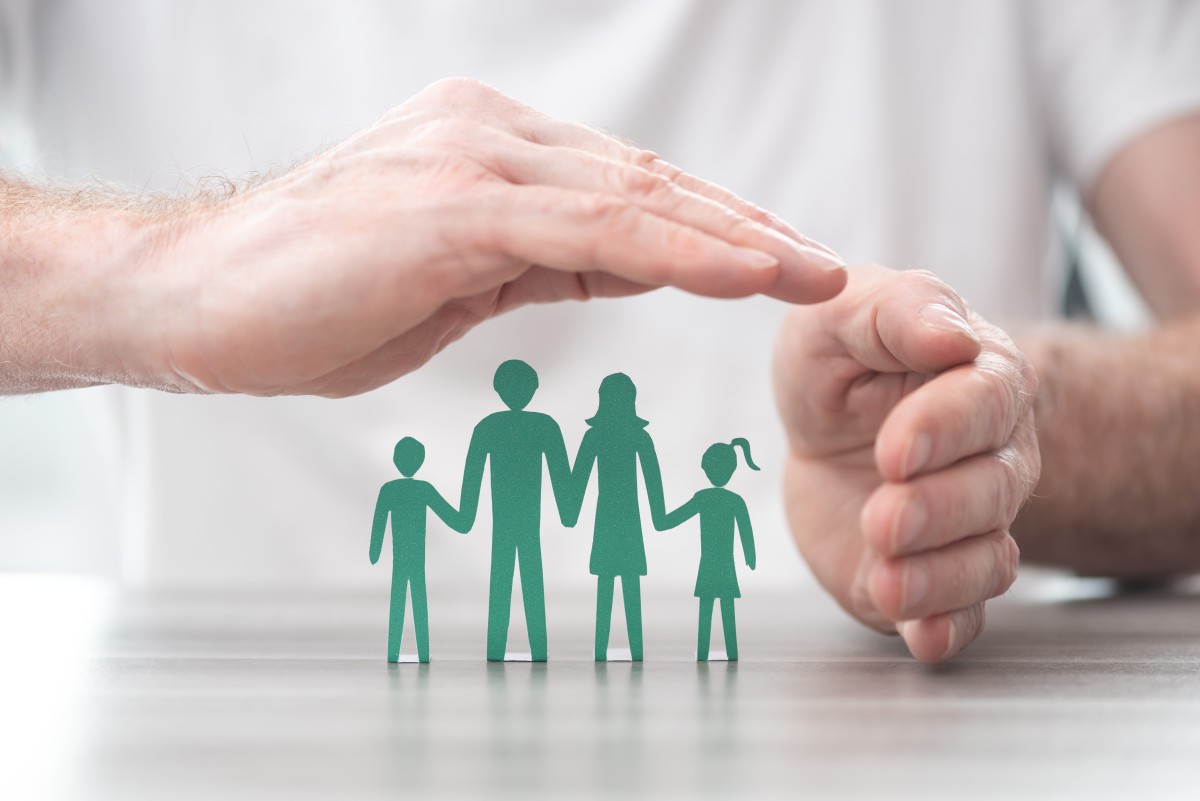 Man's hands cover a paper cut out family, suggesting they are protected 290457243