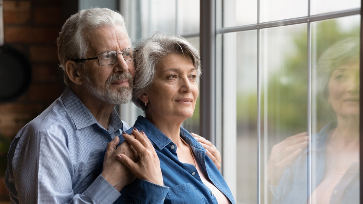 older couple looks out window, man stands behind woman with hands on shoulders422121134