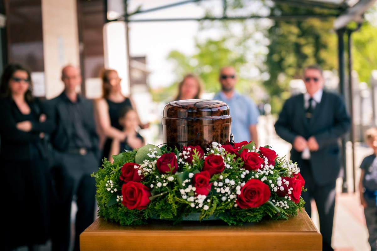funeral urn surrounded by flowers while mourners look on 433589043