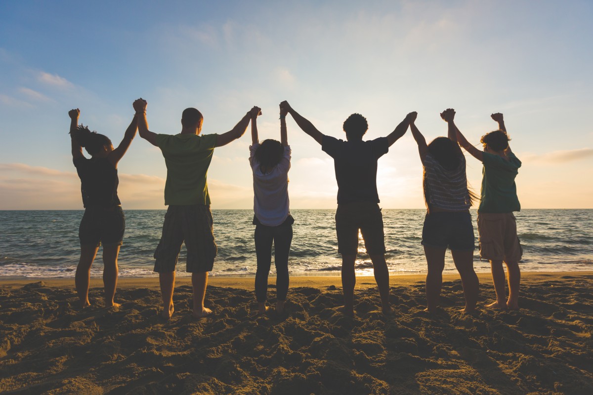 group of people stand on beach holding hands at sunset78597407