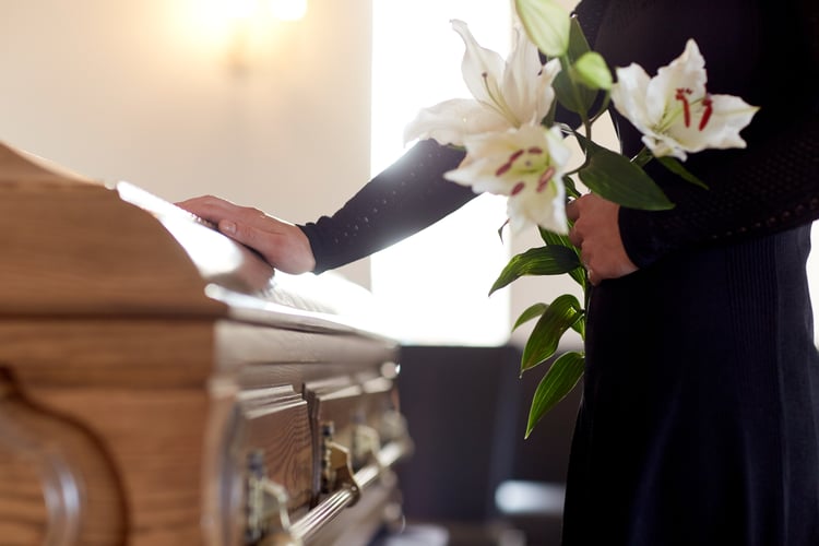 Person holding flowers at funeral casket